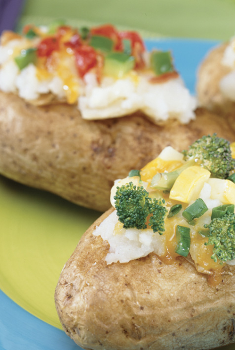 Two baked potatoes topped with cheese and vegetables on a blue plate.