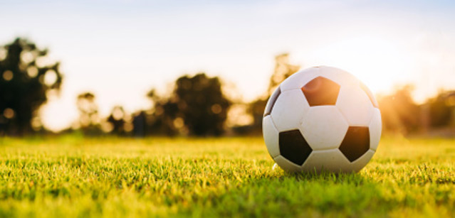 A soccer ball on grass with the sun in the background.