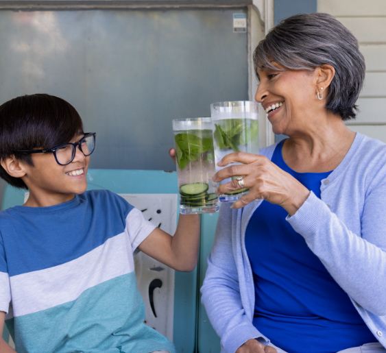 A woman and a boy smiling, toasting with glasses of water.