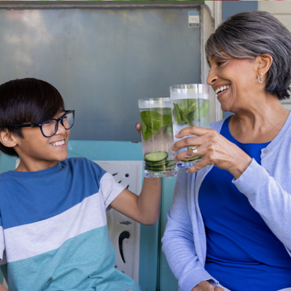 A woman and a boy smiling, toasting with glasses of water.