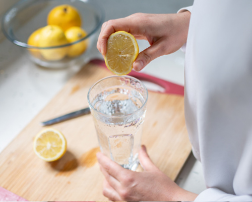 Una mano sosteniendo una rodaja de limón sobre un vaso de agua.