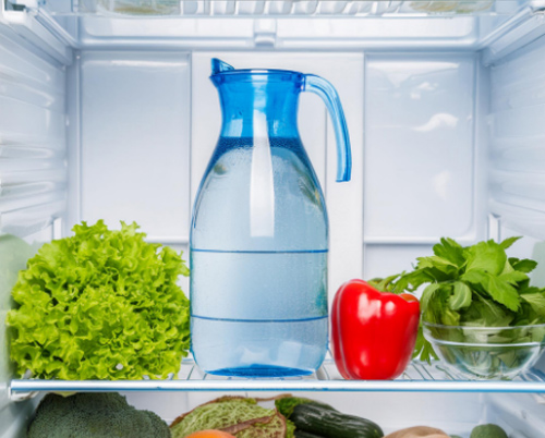 Verduras frescas y una jarra de agua en un refrigerador.