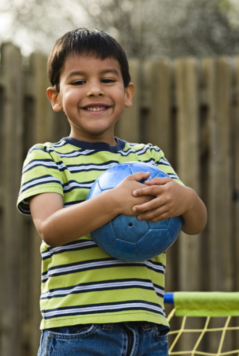 Un niño pequeño con cabello corto y castaño, sosteniendo una pelota azul en sus manos.