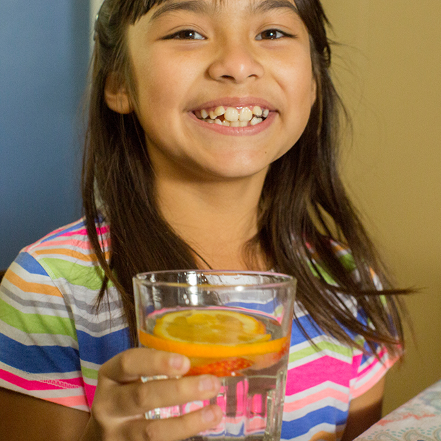  Una niña sonriente con un vaso de agua con una rodaja de naranja 